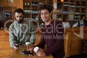 Two male friends using mobile phone while having coffee