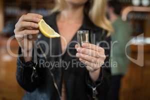 Woman holding tequila shot and lemon wedge in bar