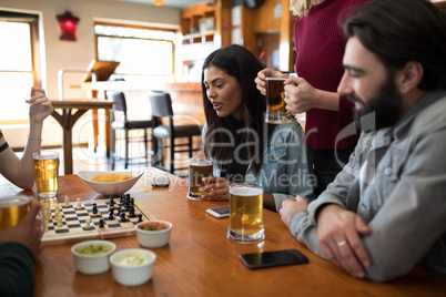 Friends playing chess while having glass of beer in bar