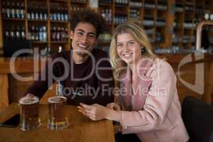 Smiling couple using mobile phone while having glass of beer in bar