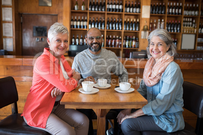 Happy friends sitting together with cup of coffee on table