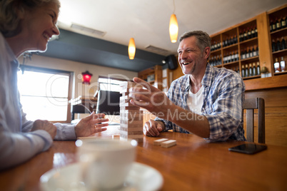 Senior friends playing jenga game on table in bar