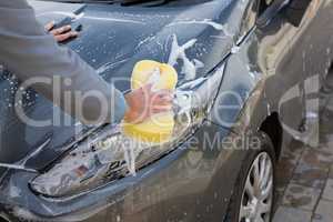Auto service staff washing a car bonnet with sponge