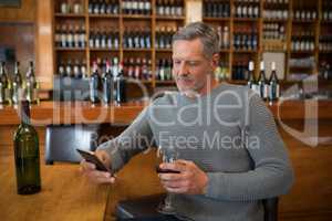 Smiling senior man using mobile phone while having red wine