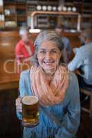 Smiling senior woman holding glass of beer in bar