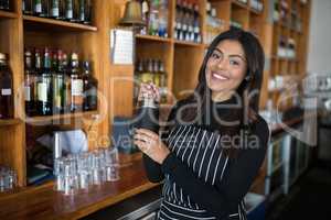 Smiling waitress shaking cocktail at bar counter in bar