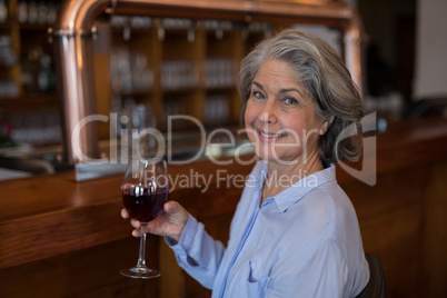 Smiling senior woman having glass of red wine at counter