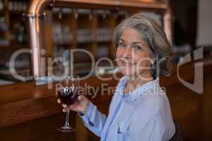 Smiling senior woman having glass of red wine at counter