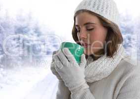 Woman wearing gloves and hat drinking from cup in snow forest