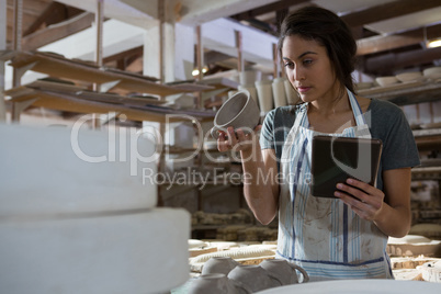 Female potter holding cup while using digital tablet