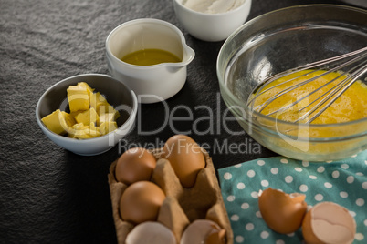 Beaten eggs, egg tray, butter, oil and flour kept on a black surface