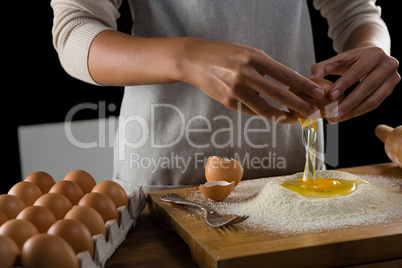 Man breaking eggs in the flour on wooden board