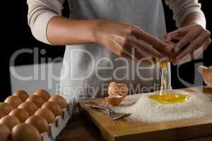 Man breaking eggs in the flour on wooden board