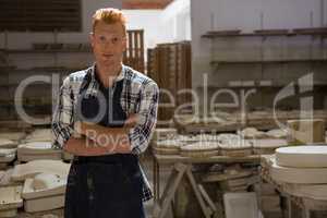 Male potter standing with arms crossed in pottery workshop