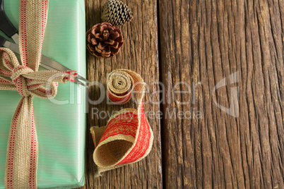 Scissors, pine cones and ribbon with wrapped gift box on wooden table