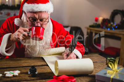 Santa Claus having coffee while writing on scroll