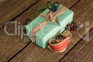 Scissors, pine cones, leaves and ribbon with wrapped gift box on wooden table