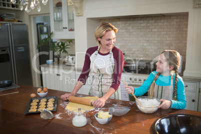 Smiling mother and daughter preparing cookies in kitchen