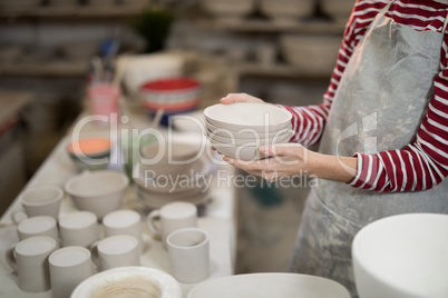 Mid section of female potter holding stack of bowls