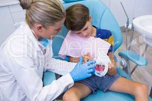 Dentist teaching boy brushing teeth on dentures at medical clinic
