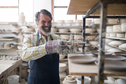 Happy male potter placing plate ob shelf