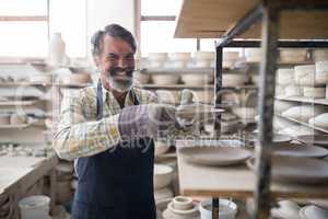 Happy male potter placing plate ob shelf