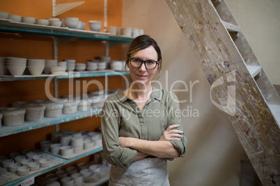 Female potter standing with arms crossed in pottery workshop