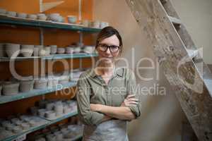 Female potter standing with arms crossed in pottery workshop