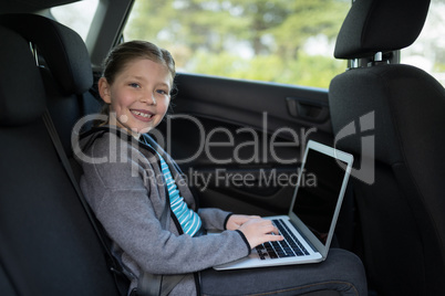 Teenage girl using laptop in the back seat of car