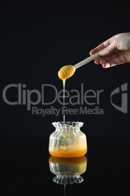 Honey dipper with flowing honey in glass jar