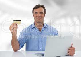 Businessman at desk with laptop with bright background and bank card