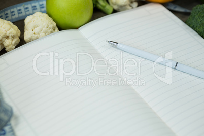 Open diary with vegetables on wooden background