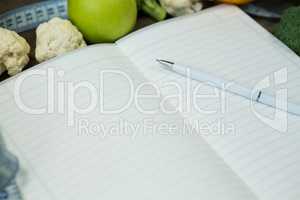 Open diary with vegetables on wooden background