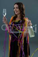 Smiling woman wrapped in multi color streamers holding champagne