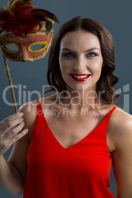 Woman holding masquerade mask against black background