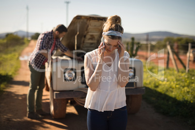 Woman talking on mobile phone while man repairing a car