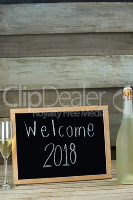 Champagne bottle and glass kept beside the slate with welcome 2018