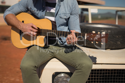 Man playing guitar while sitting on a car