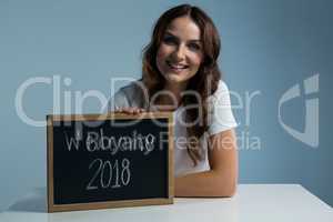 Smiling woman showing slate with text welcome 2018 against grey background