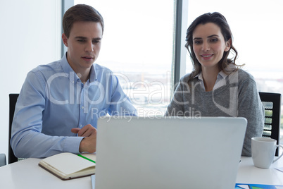 Male executive and female executive working over laptop