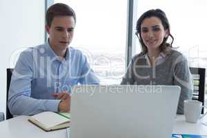 Male executive and female executive working over laptop
