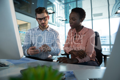 Executives discussing over glass digital tablet at desk