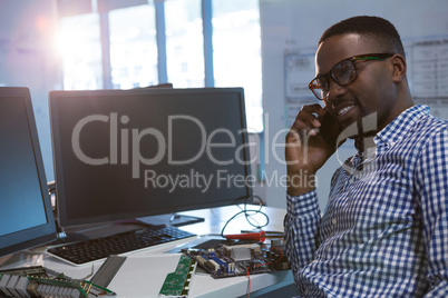 Computer engineer talking on mobile phone at desk