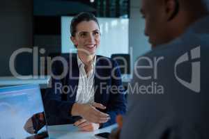 Smiling female executive offering handshake at desk