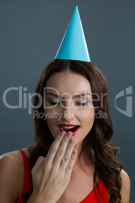 Woman in party hat yawning against black background