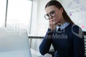 Thoughtful female executive using laptop at desk