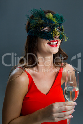 Woman wearing masquerade mask and having glass of champagne