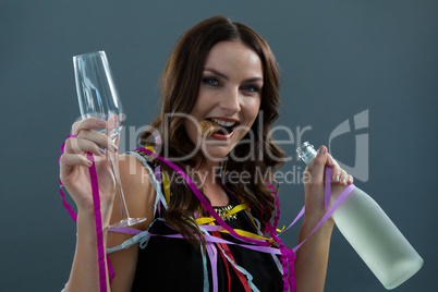 Smiling woman wrapped in multi color streamers holding champagne bottle and glass