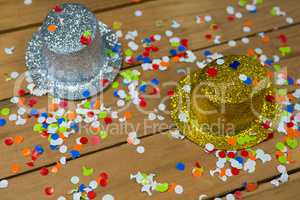 Golden and silver hat with confetti on wooden surface