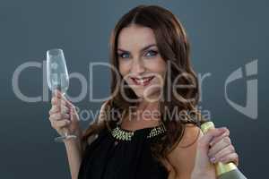 Smiling woman holding champagne bottle and glass against grey background